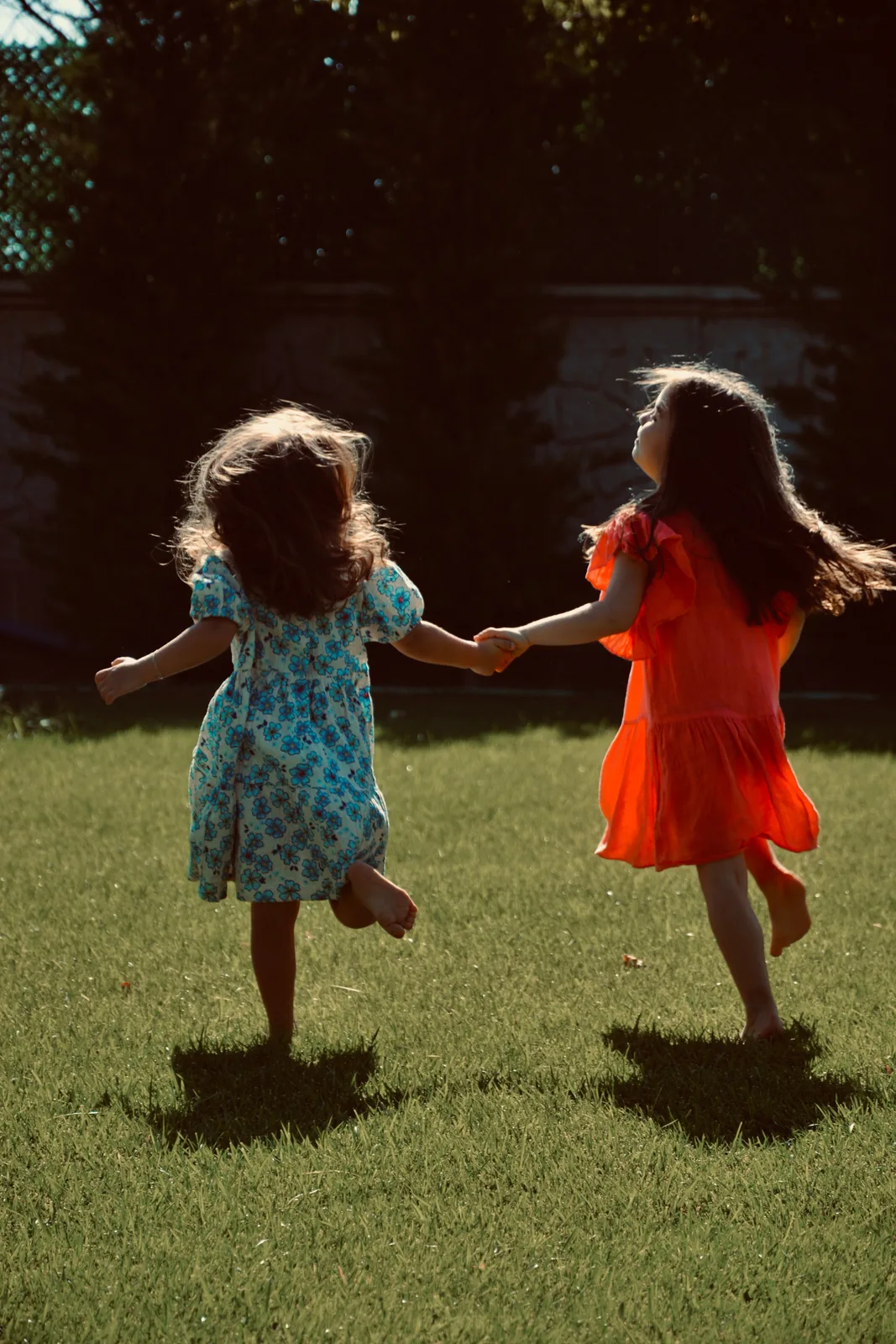 Two girls running hand in hand across the grass