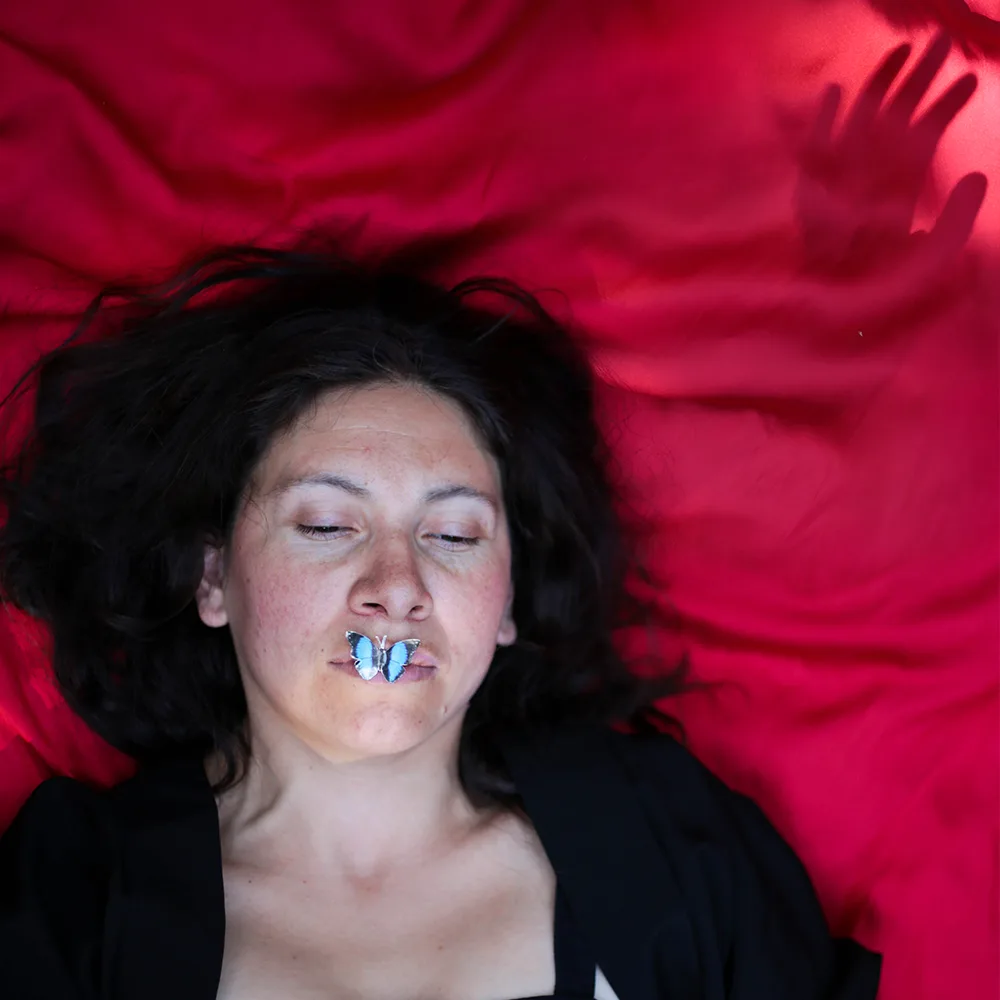 A woman lying on red fabric with a butterfly on her lips